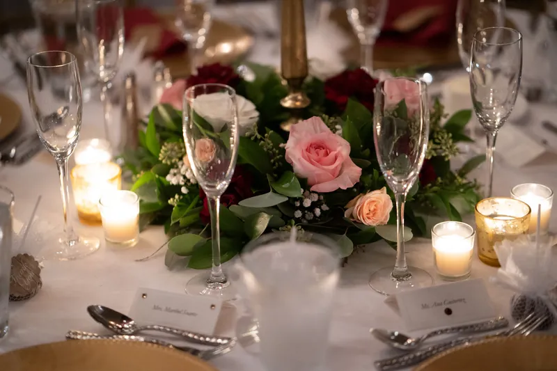 Intimate table setting with pink and coral rose centerpiece, champagne flutes, and candles under warm lighting.