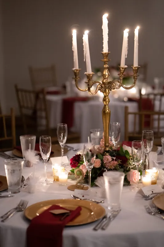 Gold candelabra with lit white candles anchors a reception table decorated with pink roses and burgundy accents.