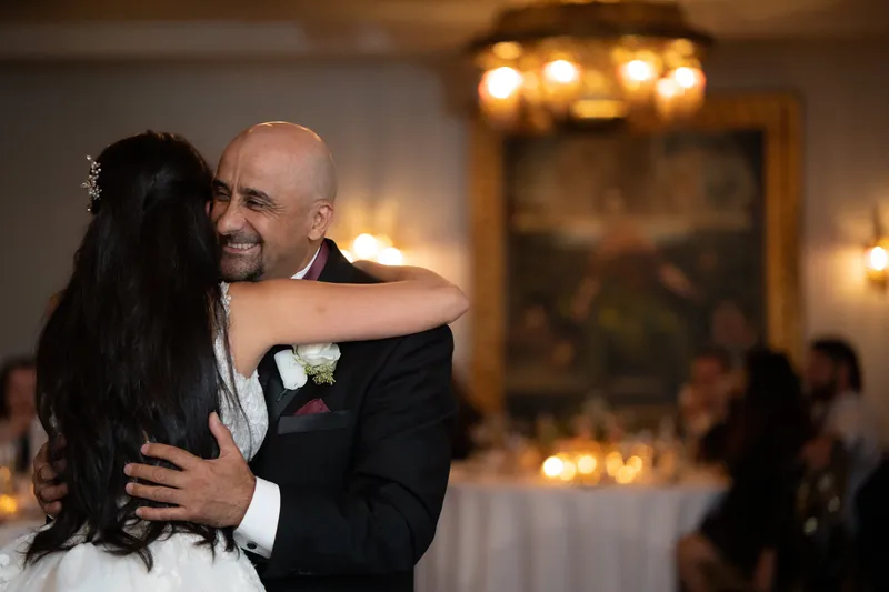 Michael embraces Monica in her white wedding dress under warm ambient lighting during their first dance.