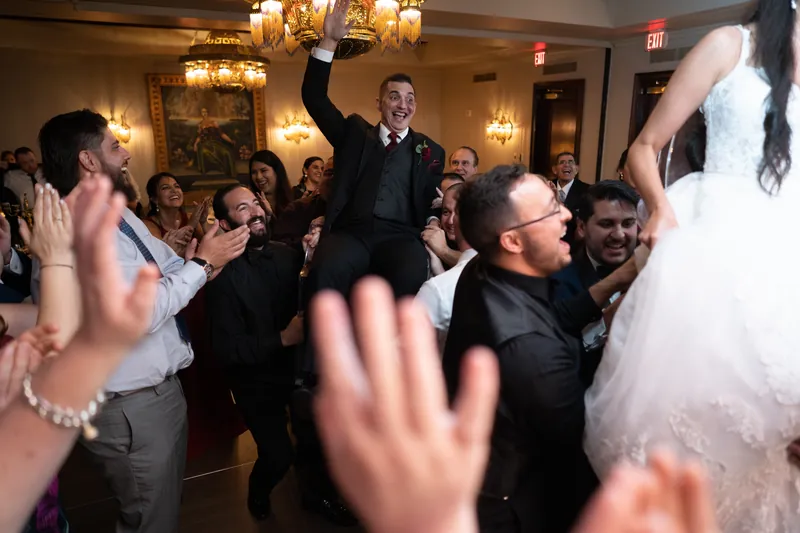 Michael raises his fist triumphantly on the dance floor surrounded by celebrating guests and Monica in white tulle.
