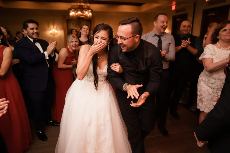 Monica and Michael dancing together surrounded by guests in the warmly lit ballroom.