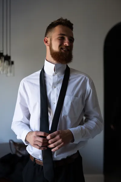 Man in formal attire holding black tie in modern interior setting