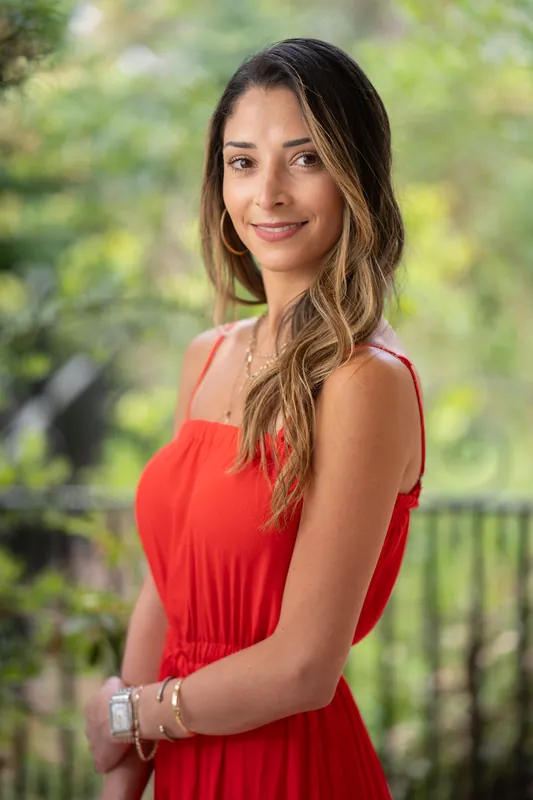 Natasha wears a flowing red dress and smiles at the camera against a lush green backdrop at Casa Futrell.