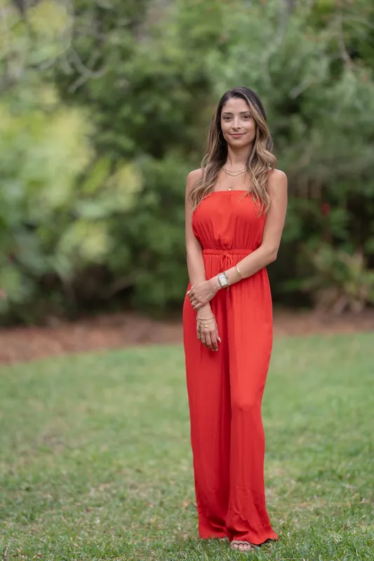Natasha stands alone in a red sleeveless gown against lush greenery at Casa Futrell, smiling with hands clasped at her side.