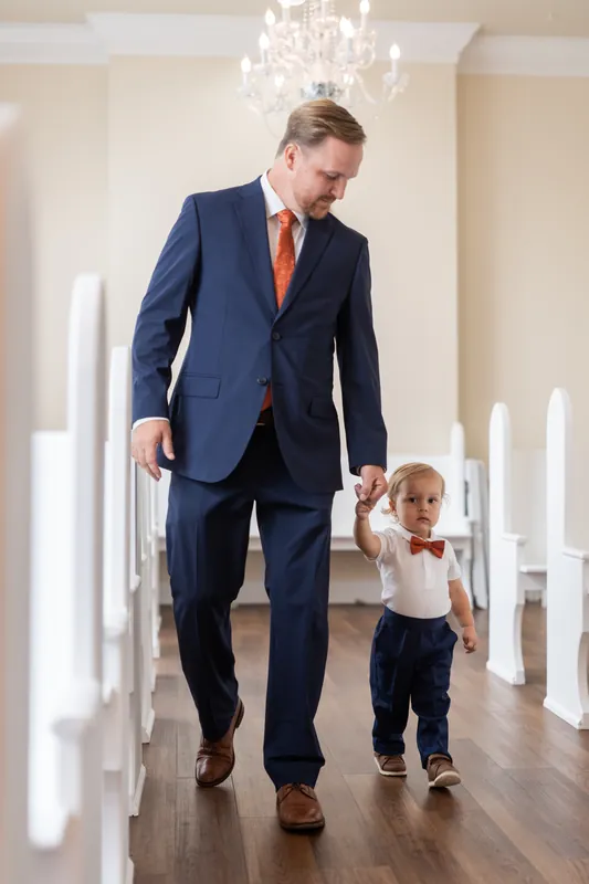 Nathan and a young child walk hand-in-hand down a hallway lined with white candles at Lightner Museum.