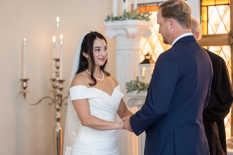 Nathan and Hillary hold hands at the altar in Lightner Museum's elegant chapel, with golden stained-glass windows and candles glowing behind them.
