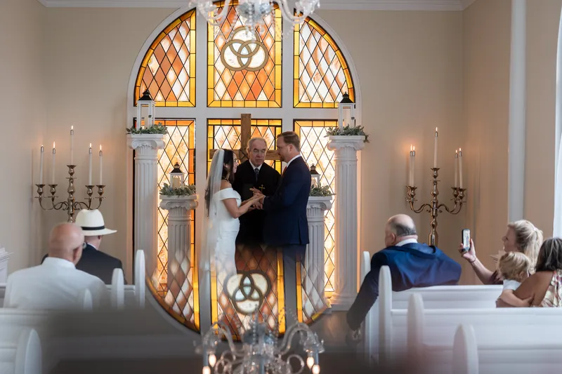 Two people stand together during their ceremony as guests watch from wooden pews, framed by the chapel's distinctive geometric stained-glass window.