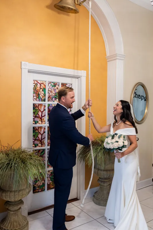 Nathan and Hillary exchange a high-five in the museum's yellow corridor, both beaming in their wedding attire beneath stained glass.