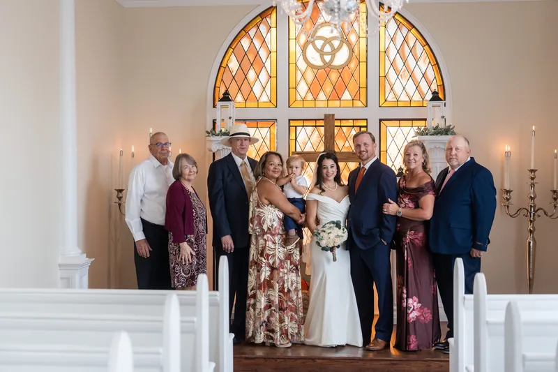 Eight guests pose together in the museum's chapel, framing a couple in wedding attire with white columns and golden stained glass behind them.
