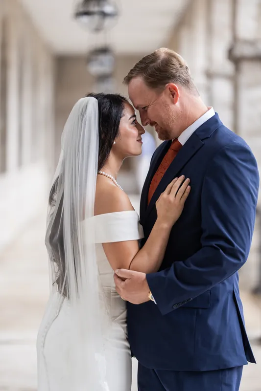 Couple facing each other closely in the stone arcade, both smiling during an intimate moment.
