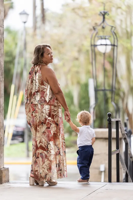 A woman in a patterned rust dress walks with a small child down a bright colonnade at the Lightner Museum.