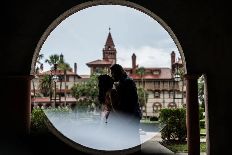 Nikki and Kiel framed through a circular archway with a Spanish colonial building and palm trees in the background.
