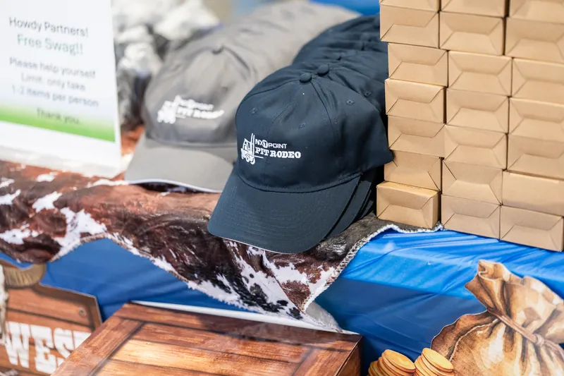 NXTPoint Pit Rodeo branded navy cap and merchandise displayed on a table with stacked boxes at an event.