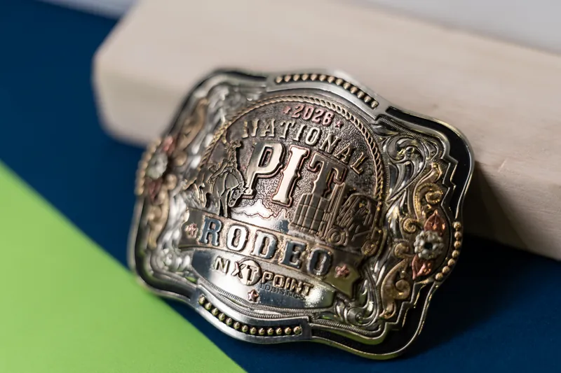 Close-up of an ornate silver rodeo belt buckle with detailed embossing resting on a white and blue surface.