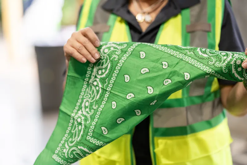 Someone in a lime-green safety vest holds up a green bandana with white skull pattern.