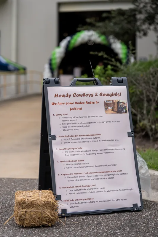 A sandwich board sign advertising "Howdy Cowboys & Cowgirls" sits on pavement beside a hay bale at Jacksonville Beach, St. Augustine.