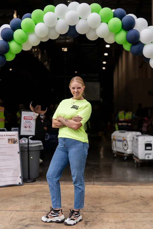 Someone in a neon yellow shirt stands beneath a green, white, and navy balloon arch at the outdoor event.