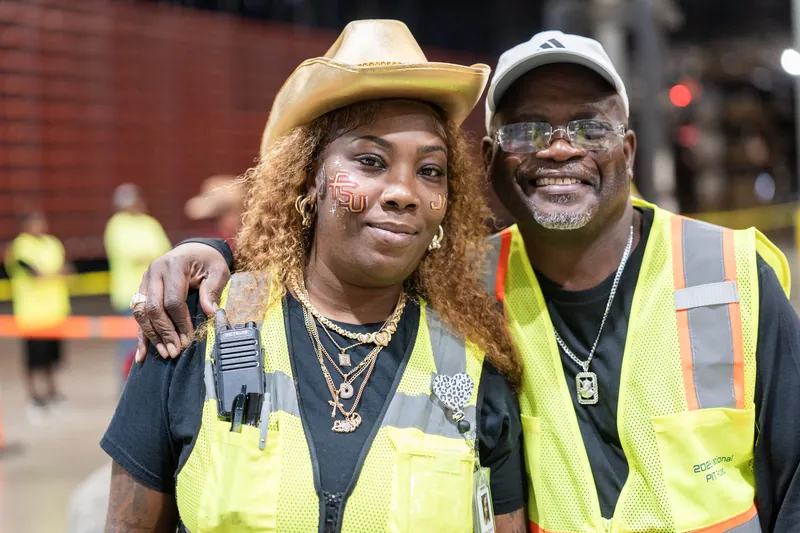 Two people wearing bright yellow safety vests and chains pose together, smiling at the camera during the rodeo event.