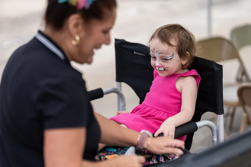 An event staff member in a black shirt helps a small child in a bright pink dress during an activity.