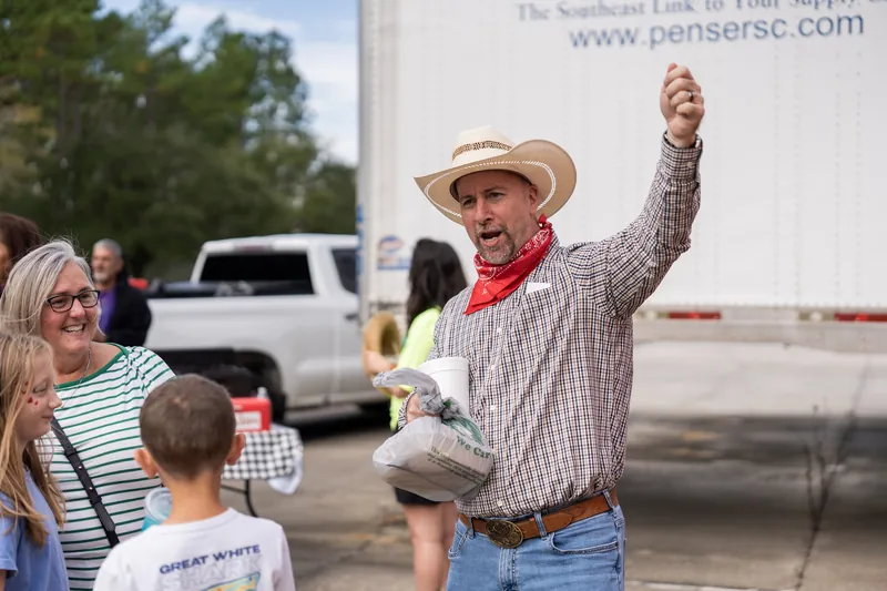 A man in a tan cowboy hat and red bandana raises his fist while speaking to a small group at the event.