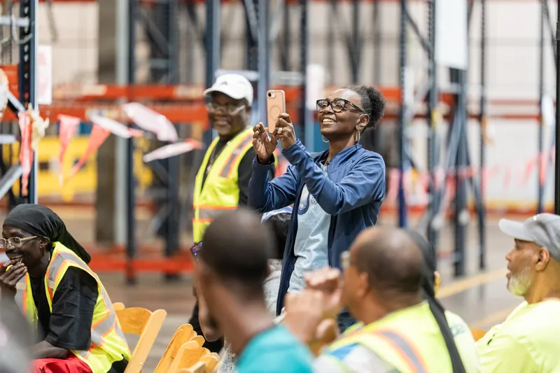 Spectators in hard hats and safety vests watch and photograph the action unfolding at the Jacksonville Beach event venue.