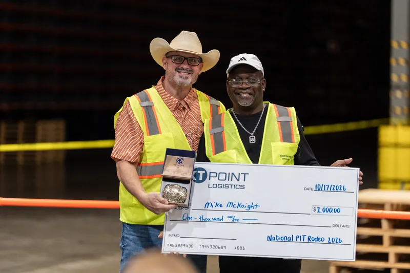 Two participants in bright safety gear proudly hold a large ceremonial check at Jacksonville Beach pit rodeo awards ceremony.