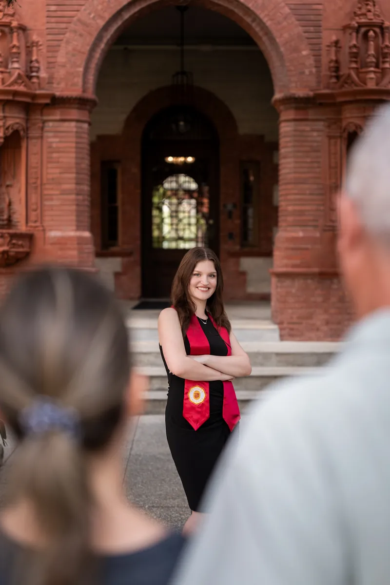 Woman in red and black outfit standing on brick steps, seen from behind with two people partially visible in the foreground.