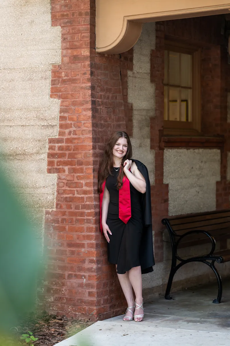 Olivia stands in a doorway in a black dress and red scarf against red brick and cream-colored building facade