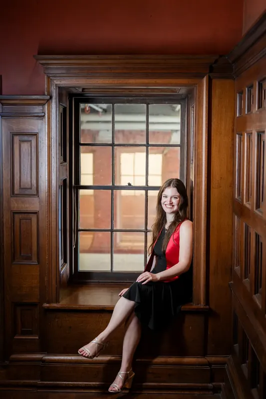 Olivia sits on a wooden window ledge, backlit by gridded panes in the period architecture of Flagler College.