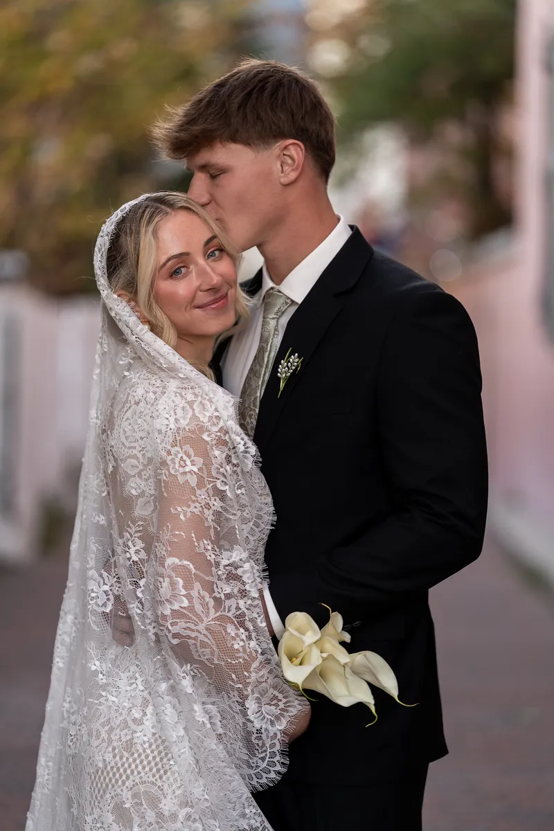 Paige tilts her head toward Owen's shoulder while he gazes down at her, both holding bouquets in the historic district's soft