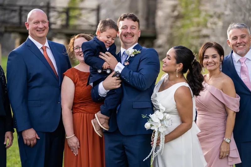Two people in wedding attire stand with family members at Castillo de San Marcos, one holding a small child in a navy suit.
