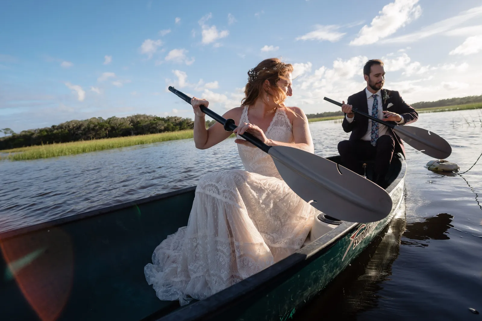 Bride and groom paddling canoe together in wedding attire