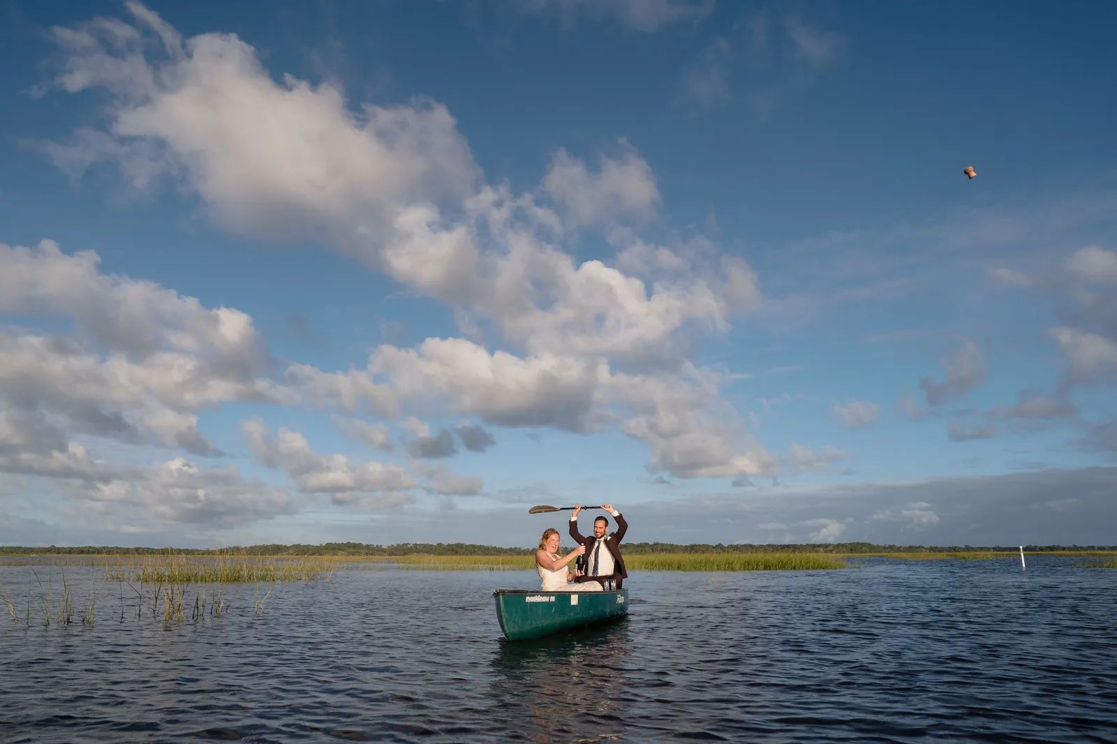Wide shot of couple in canoe raising paddle in celebration