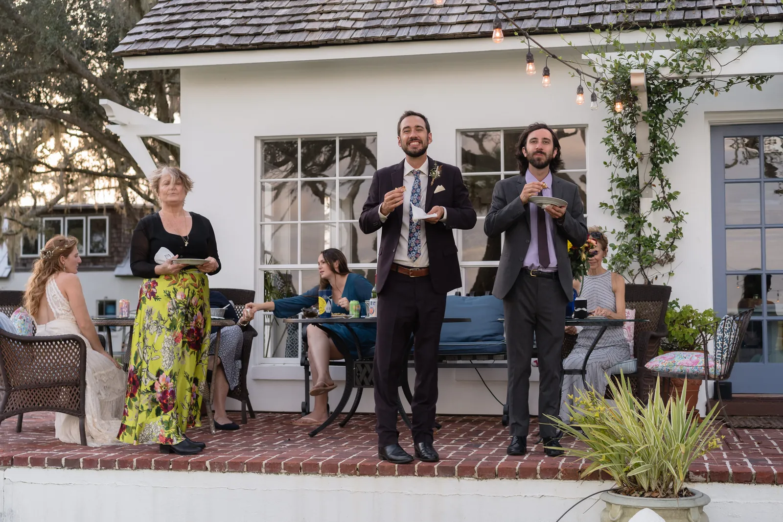 Groom and best man eating on patio with string lights