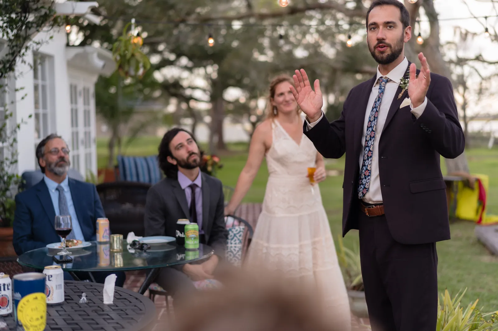 Groom giving toast while bride watches and family listens