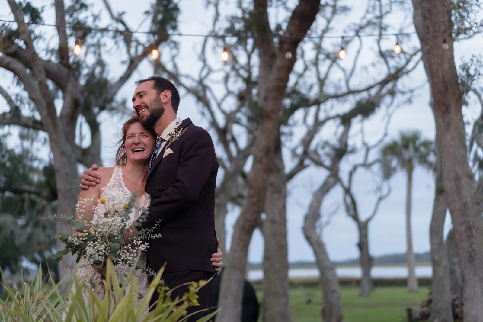 Couple laughing under string lights with wildflower bouquet