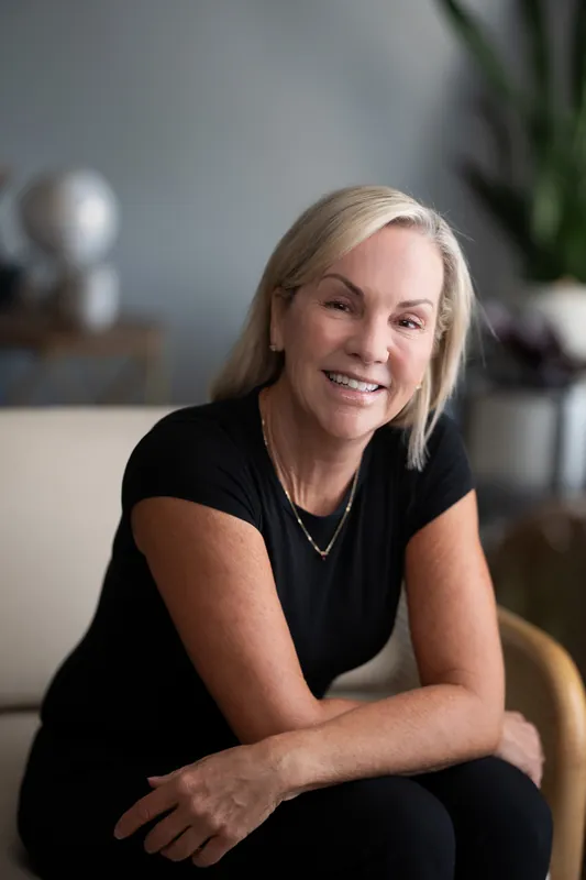 Paula Seymour sits with arms crossed, smiling at the camera in a black cap-sleeve top at Casa Futrell in St. Augustine.