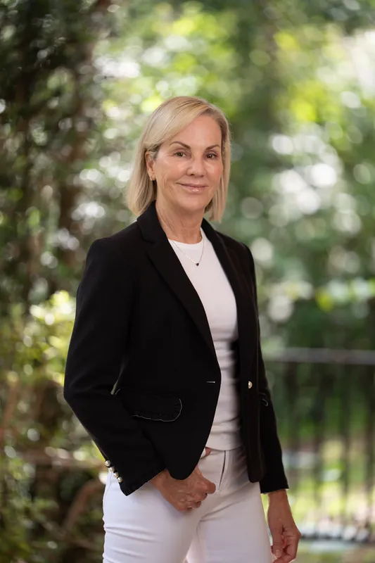 Paula Seymour stands outdoors at Casa Futrell with hands in jacket pockets, wearing a black velvet blazer over a white top.