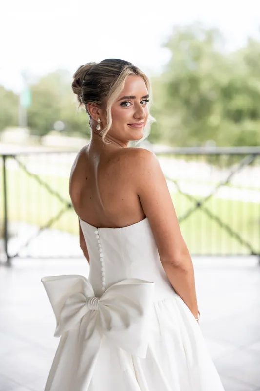 A person in a white wedding dress with a bow detail on the back looks over their shoulder on a sunny balcony at Crosswater Hall at Nocatee, Jacksonville.