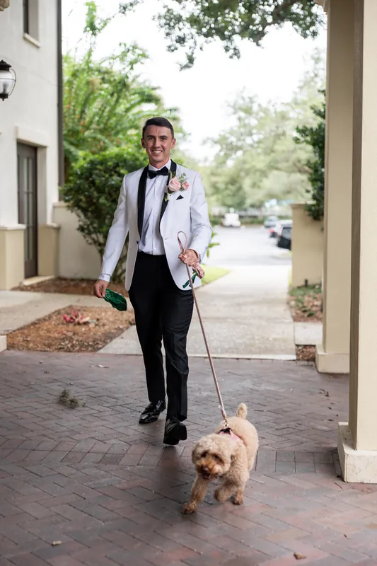 Someone in a light suit and bow tie walks a small tan dog along a brick pathway at Crosswater Hall at Nocatee, Jacksonville.