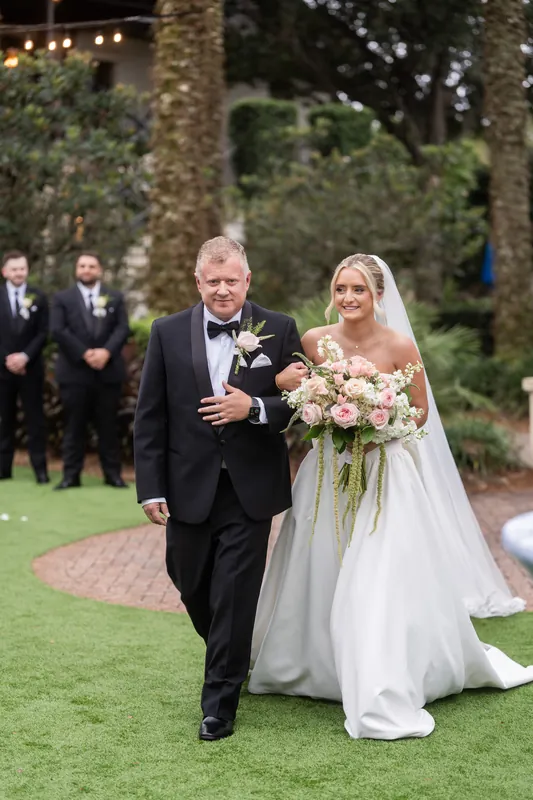 Two people walk down the aisle together on manicured grass lined with white chairs at Crosswater Hall at Nocatee.
