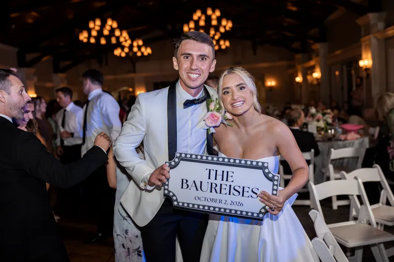 Payton and Tyler hold a marquee sign reading "The Baucisses" while posing together at their wedding reception.
