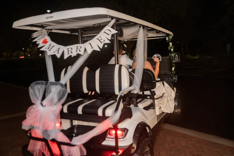 Decorated golf cart with striped balloon arch and pink bows sits parked outside the venue at night.