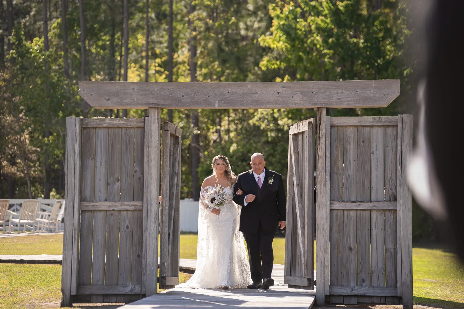 Bride Riley walking with father through rustic barn doors at Tringali Barn