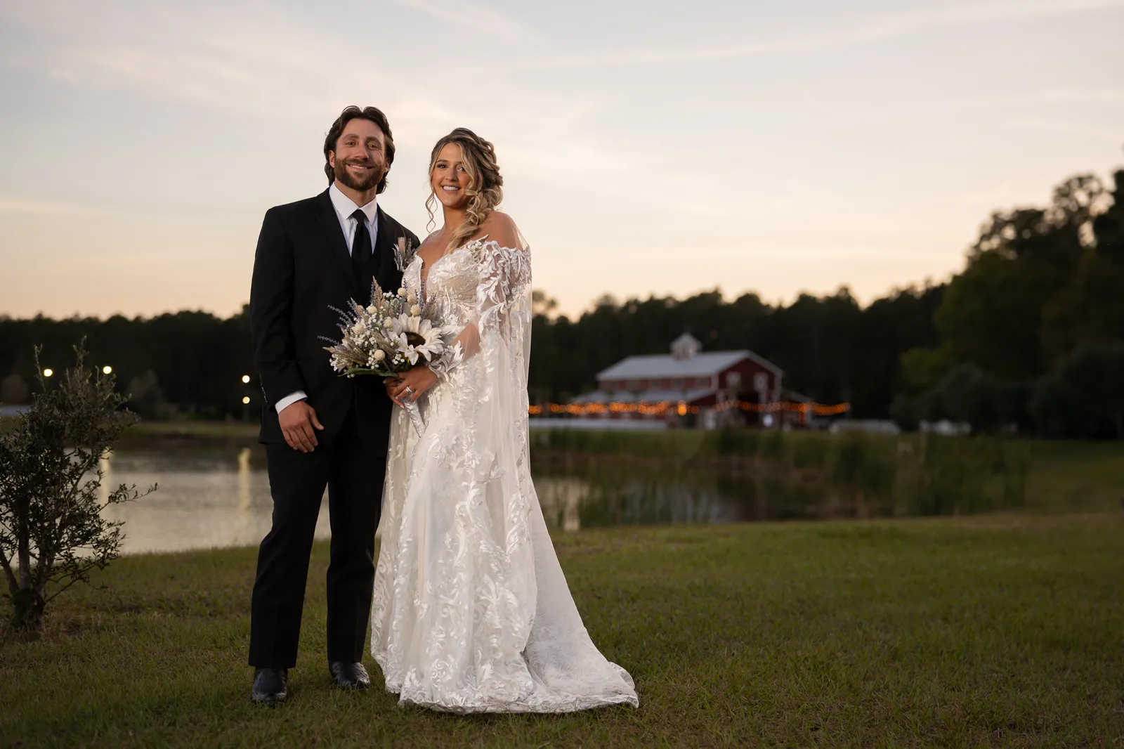 Bride and groom posing together in field at sunset with barn