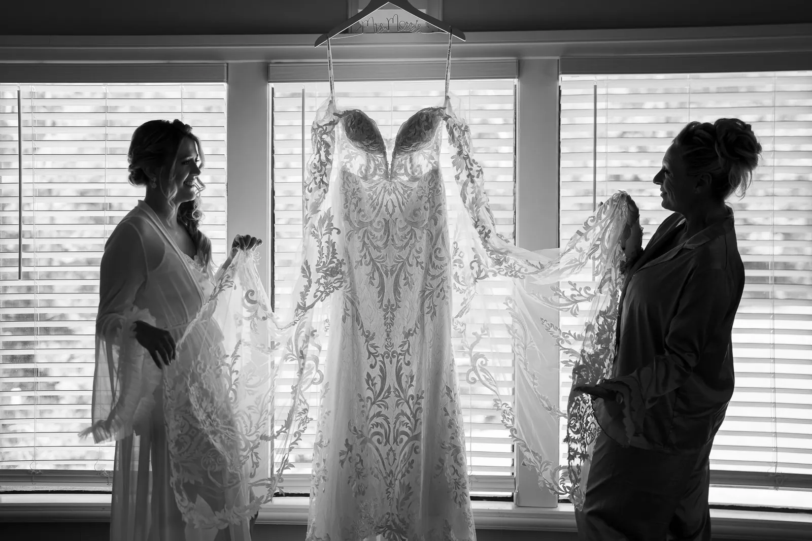 Wedding dress hanging in window with bride and mother black and white at Tringali Barn