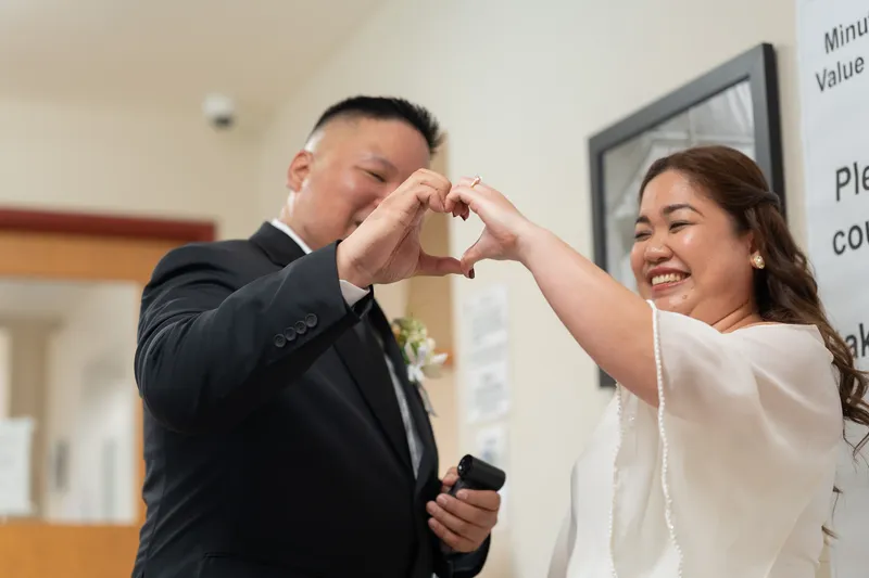 Ronald and Vanessa share a sweet moment making a heart shape with their hands together, both smiling joyfully.