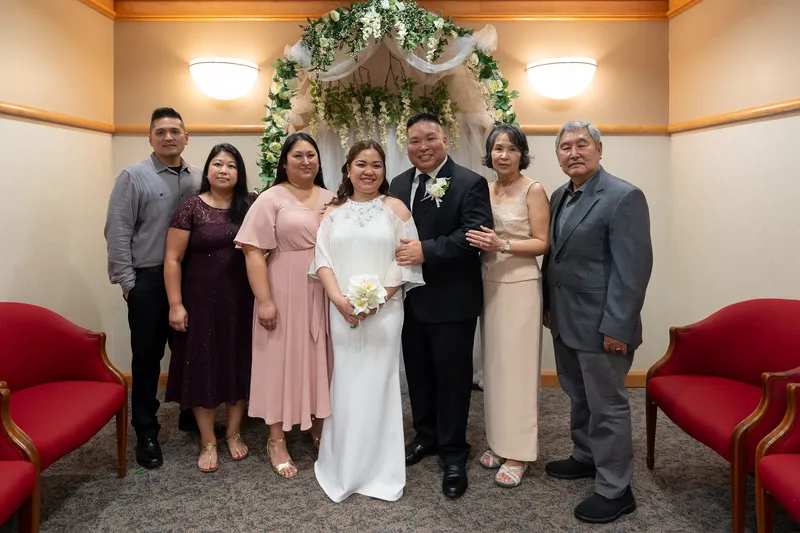 Ronald and Vanessa pose with their wedding party and family members in front of a floral arch after their intimate ceremony.