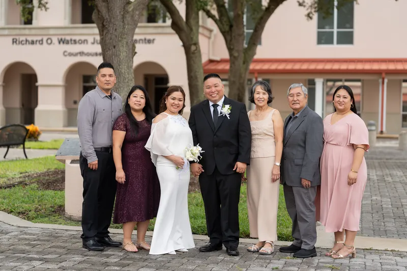 Ronald and Vanessa pose with their wedding party and family members in formal attire outside a courthouse building after their ceremony.