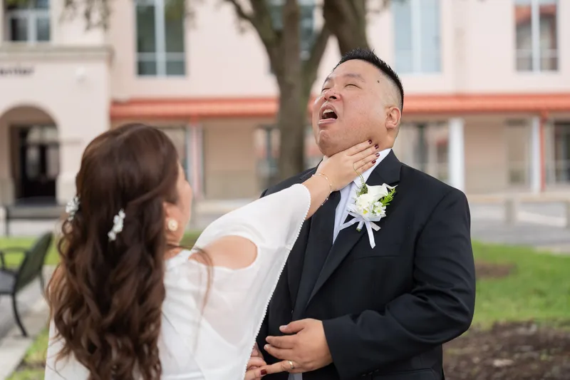 Ronald throws his head back in joyful laughter as Vanessa lovingly reaches up to touch his face during their wedding day portraits.